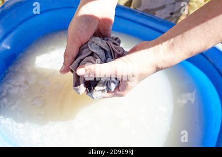 Lavaggio manuale delle mani. Primo piano di lavanda donna lavanderia in plastica blu bacino esterno. Le mani femminili lavano i vestiti in acqua saponata Foto Stock