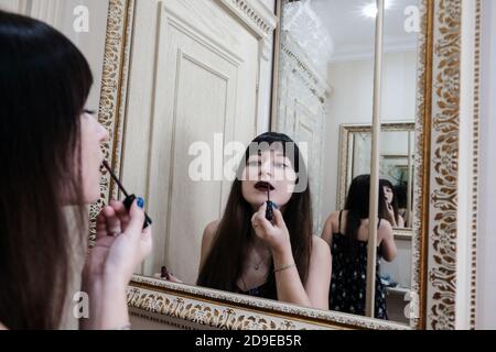 Giovane donna che applica il rossetto davanti ad uno specchio. Ragazza che si prepara con il suo trucco in un bagno d'albergo. Labbra pittoriche piuttosto femminili Foto Stock