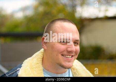 Un giovane sorridente e amichevole con una barba che guarda via all'aperto in una fresca giornata autunnale da vicino Foto Stock