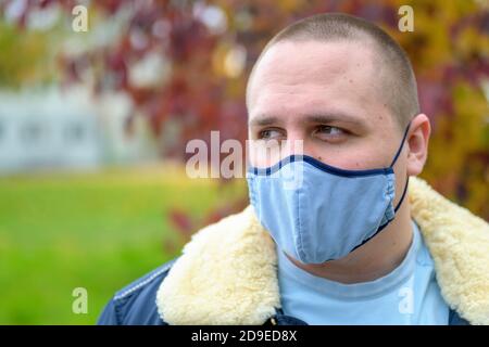 Giovane uomo casual in una calda giacca autunnale che cammina all'aperto indossare una maschera facciale in tessuto per il controllo delle infezioni durante il Covid-19 o pandemia di coronavirus Foto Stock