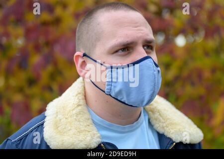 Giovane uomo casual in una calda giacca autunnale che cammina all'aperto indossare una maschera facciale in tessuto per il controllo delle infezioni durante il Covid-19 o pandemia di coronavirus Foto Stock