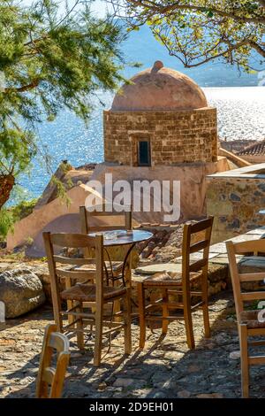 Caffè tradizionale esterno nel castello medievale fortificato di Monemvasia. Tavoli in ferro e sedie in legno con vista sulla chiesa di San Nicola e sul Foto Stock