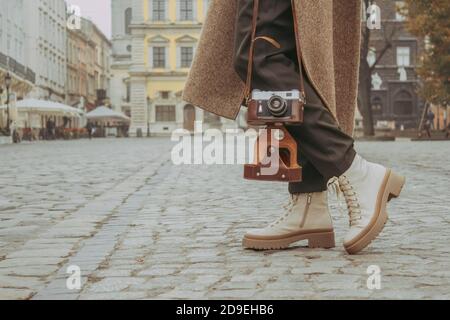 Immagine senza volto di giovane donna elegante - viaggio blogger a piedi lungo la strada centrale della città utilizzando vecchia fotocamera vintage. Autunno o primavera