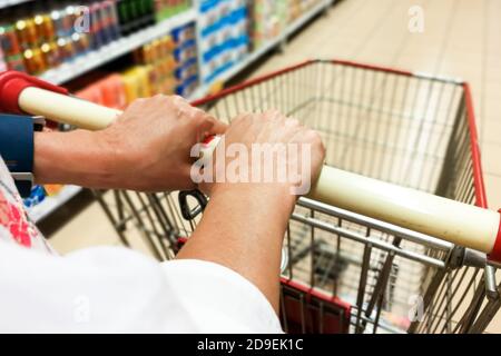 Persona che spinge il carrello del carrello dello shopping contro lo sfondo moderno corridoio del supermercato Foto Stock