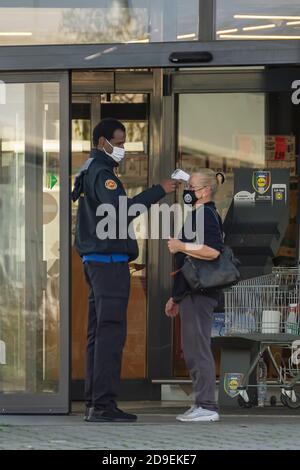 Un responsabile della sicurezza misura la temperatura di un cliente con un digitale termometro a infrarossi per fronte all'ingresso di un supermercato Foto Stock