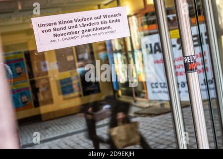 Freiburg im Breisgau, Germania. 05 novembre 2020. Due persone con bocche e nasi coperti di fronte ai loro volti oltrepassano l'ingresso di un cinema, al quale un foglio di carta con l'iscrizione 'i nostri cinema rimangono chiusi su richiesta dei governi federali e statali. Il 1° dicembre vedremo e di nuovo! A causa di un forte aumento del numero di casi, il governo federale e la Länder hanno deciso un blocco parziale per il mese di novembre, che interesserà in particolare ristoranti e istituzioni culturali. Credit: Philippe von Ditfurth/dpa/Alamy Live News Foto Stock