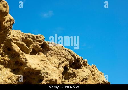 Texture rock su uno sfondo di cielo blu. La struttura perforata porosa della pietra. Rocce costiere. Foto Stock