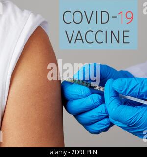 primo piano di un medico, indossando un cappotto bianco e guanti chirurgici blu, vaccinando un giovane uomo caucasico, e il testo vaccino covid-19 Foto Stock