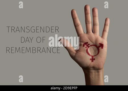 il closeup della mano di una persona, con un simbolo transgender dipinto in esso, e il testo transgender giorno del ricordo su uno sfondo grigio Foto Stock
