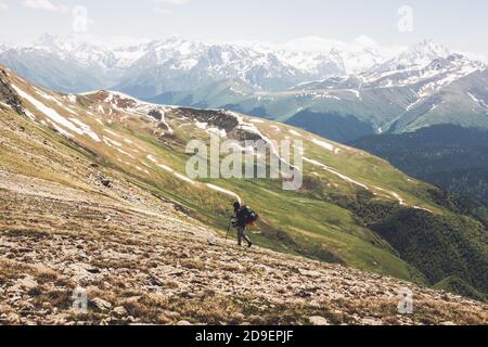 Il viaggiatore in salita con uno zaino pesante e bastoni sale fino alla cima della montagna coperta di erba e neve. Concetto di conquista delle vette e di divertimento Foto Stock