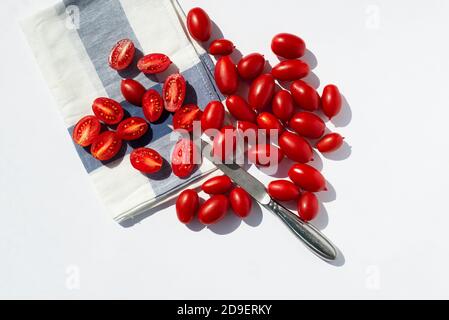 Pomodori ciliegini rossi su un tovagliolo da cucina e un coltello in acciaio su sfondo bianco. Pomodori interi e tagliati a metà. Spazio di copia per il testo. Foto Stock