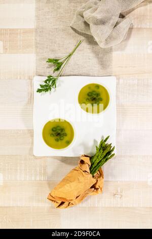 Vista dall'alto di una zuppa di verdure doppio piatto con prezzemolo e asparagi freschi in un sacchetto di carta su un tavolo di legno. Concetto di cibo sano e vegano. Foto Stock
