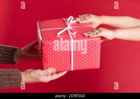 mani di un adulto che tiene fuori una scatola rossa del regalo Per Natale o compleanno Foto Stock