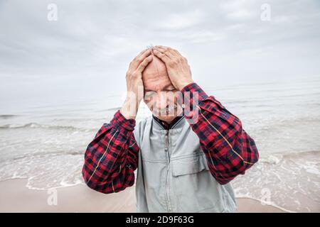 Uomo anziano che soffre di mal di testa su sfondo marino giorno nebbia Foto Stock