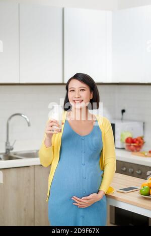 Donna incinta beve il latte sulla cucina della casa. Foto Stock