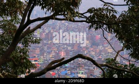 Vista del centro densamente popolato di Kathmandu, Nepal con edifici colorati attraverso i rami di albero dalla cima del tempio complesso Swayambhunath. Foto Stock