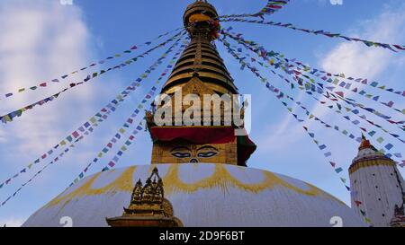 Vista frontale della cima dello stupa buddista color oro nel complesso templare Swayambhunath, Kathmandu, Nepal decorato con colorate bandiere di preghiera che volano. Foto Stock