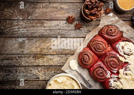 Involtini di cannella fatti in casa, velluto rosso con glassa di formaggio cremoso su sfondo di legno, vista dall'alto Foto Stock