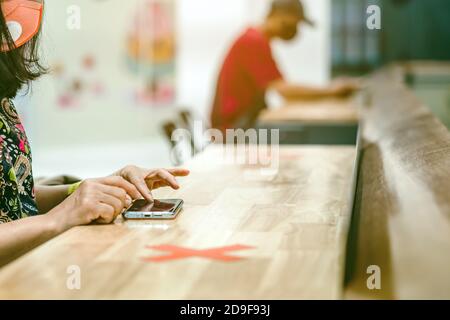 Donna che usa telefoni cellulari per lavorare con immagine sfocata di il contrassegno di posto alternativo per la distanza sociale regola la distanza per uno sedile da altre persone a. Foto Stock