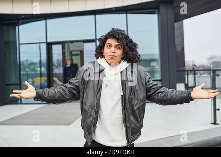 Bell'uomo giovane con capelli neri ricci che posano per macchina fotografica sulla strada contro l'edificio Foto Stock