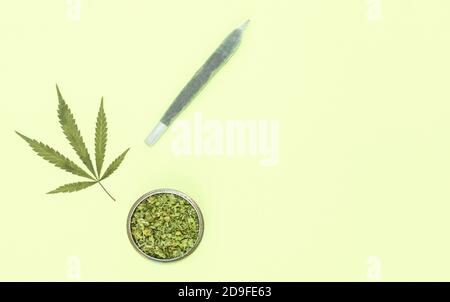 Grande giunto marijuana, macinacaffè pieno di erbacce tritate e foglia su sfondo giallo con copia spazio a destra. Foto Stock