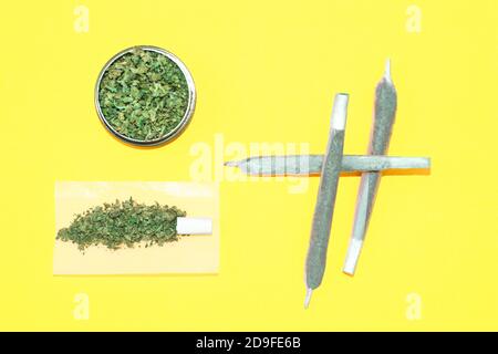 Grandi articolazioni di marijuana e macinacaffè pieno di erbacce su sfondo giallo. Foto Stock