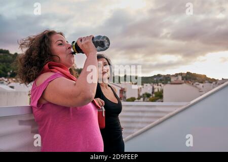 Due donne con corpi reali bevono acqua dal loro riutilizzabile bottiglie Foto Stock