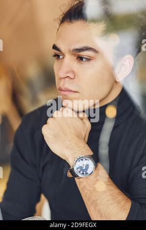 Ritratto di giovane sicuro in maglione nero che sedeva all'interno Foto Stock