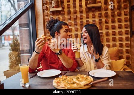 Giovane coppia multietnica che si siede all'interno insieme e mangia la pizza Foto Stock