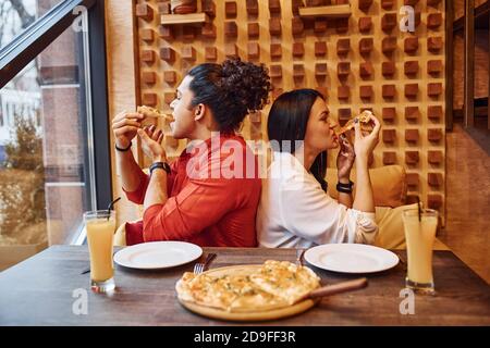 Giovane coppia multietnica che si siede all'interno insieme e mangia la pizza Foto Stock