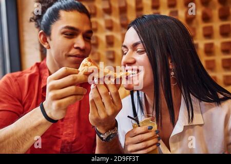 Giovane coppia multietnica che si siede all'interno insieme e mangia la pizza Foto Stock