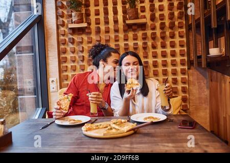 Giovane coppia multietnica che si siede all'interno insieme e mangia la pizza Foto Stock