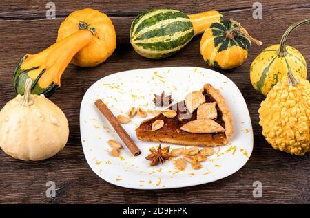 Un pezzo di crostata di zucca decorata con biscotti sotto forma di foglie con cannella, anice stellato e semi di zucca su un piatto bianco. Stile rustico. Foto Stock