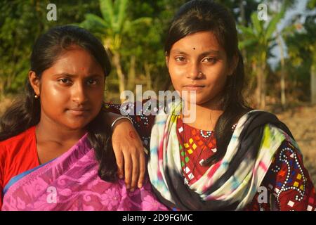 Primo piano di due belle ragazze indiane bengalesi che indossano rosato sari e salwar kameez con orecchini nasello in posa in un arato fie agricolo Foto Stock