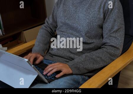 Giovane uomo che tiene il laptop in giro, che lavora su di esso, digitando in un pullover grigio con un caffè Foto Stock
