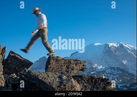 Uomo che attraversa due rocce con Mt Rainer in distanza Foto Stock