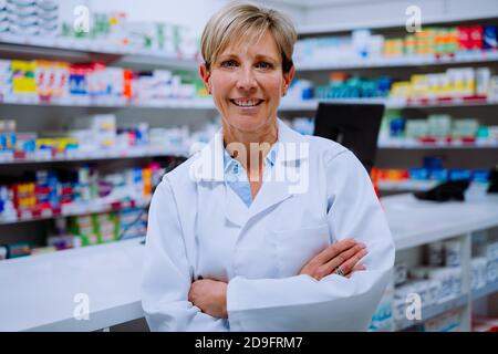 Ritratto di sorridente farmacista caucasico con braccia incrociate appoggiate contatore farmaci in farmacia Foto Stock