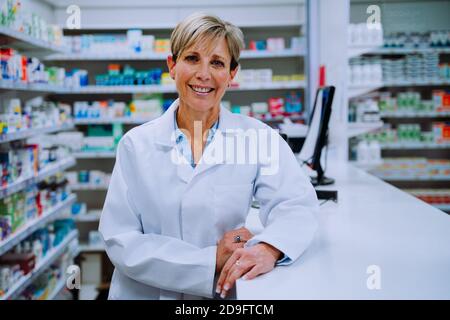 Ritratto di sorridente farmacista caucasico appoggiato contro il contatore di prescrizione in farmacia Foto Stock