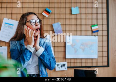 Donna d'affari sorpresa in occhiali che parlano con il cellulare nell'ufficio moderno. Foto Stock