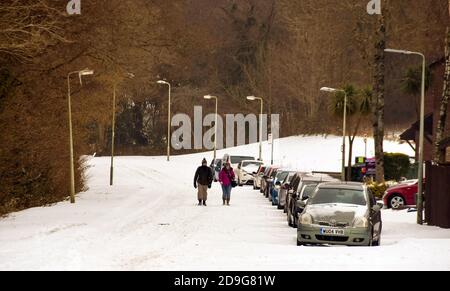 Pontypridd, Galles - Marzo 2018: Strada coperta di neve con auto parcheggiate sul lato della strada e due persone che camminano nella neve Foto Stock