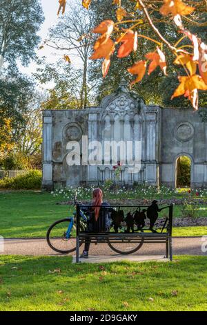 giovane donna seduta su una panchina del parco in autunno con la sua bicicletta appoggiata sul sedile o sulla panchina accanto a lei facendo un riposo su un giro in bicicletta. Foto Stock