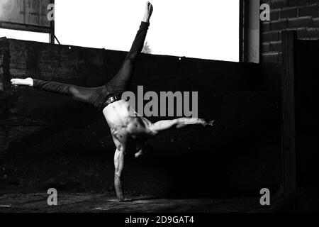 Giovane uomo che tiene l'equilibrio a portata di mano in magazzino - muscolare Modello di idoneità dell'allestitore atletico che fa il sostegno del handstand Push-up Foto Stock