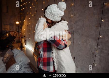 Coppia felice di stile che si abbracciano e che trascorrono insieme la vigilia di natale. Momenti accoglienti e gioiosi nelle vacanze invernali. Saluti stagionali. Concetto di pubblicità Foto Stock