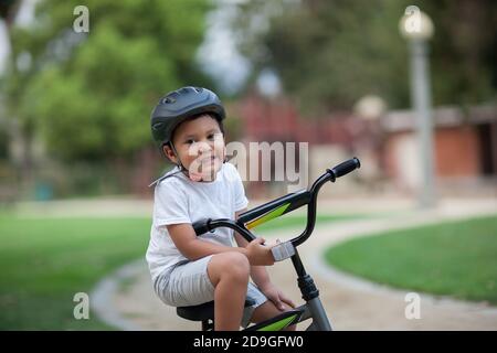 Un ragazzo sano seduto in bicicletta su un sentiero del parco che indossa un casco di sicurezza, una t-shirt e un pantaloncini. Foto Stock
