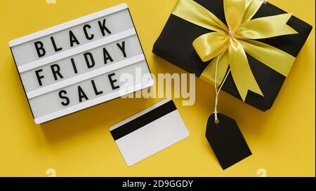 Banner concept per la celebrazione del Black Friday, lettering.White bordo con testo NERO VENDITA VENERDÌ, confezione regalo nero con arco giallo, tag, carta di credito su giallo Foto Stock
