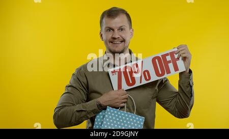 Gioioso uomo che mostra fino a 70 per cento di sconto iscrizione segno e shopping borsa, sorridente, guardando soddisfatto con prezzi bassi, shopping su grande giorno di vendita. Concetto di Black Friday Foto Stock