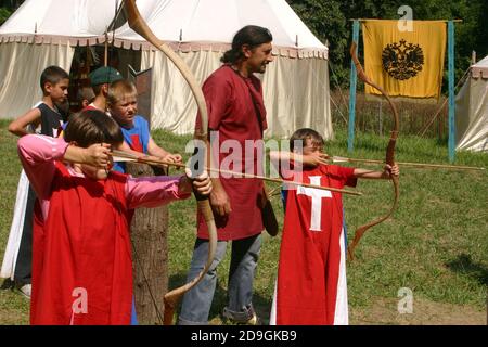 Ragazzi al campo estivo a tema medievale che vengono istruiti sull'uso l'arco e la freccia Foto Stock