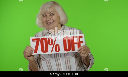 Nonna anziana che mostra fino al 70% di sconto iscrizione, pubblicità sconti, sorridente, aspetto stupito con prezzi bassi, shopping su Black Friday o Cyber Monday. Donna su sfondo chiave chroma Foto Stock