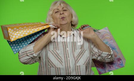 Buona nonna senior che solleva borse per la spesa, festeggiando, cercando soddisfatto con l'acquisto, godendo di sconti sulle vacanze del Black Friday. Donna anziana isolata su sfondo chiave cromatica Foto Stock