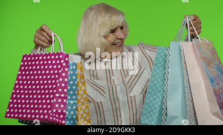 Nonna gioiosa che tiene borse per lo shopping, che esultano gli sconti in negozio, che si gode di shopping a prezzi bassi il Black Friday. Donna anziana che danzano, festeggiando su sfondo chroma chiave. Schermo verde Foto Stock